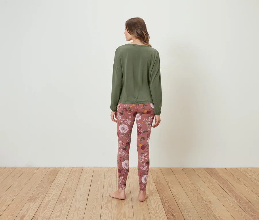 Eine Frau steht mit dem Rücken zur Kamera und trägt ein olivgrünes Langarmshirt und Leggings mit Blumenmuster.