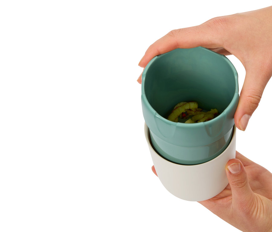 Hände halten zwei Becher, der obere ist türkis mit Inhalt, der untere ist weiß.