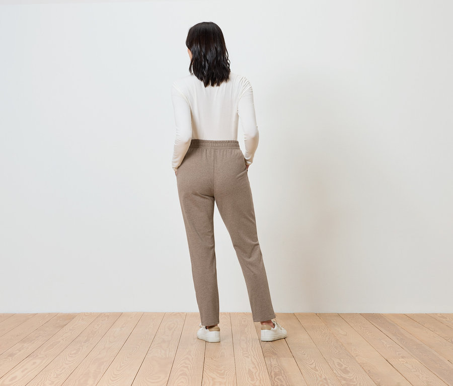 Frau von hinten trägt eine braune Hose und ein weißes Oberteil.