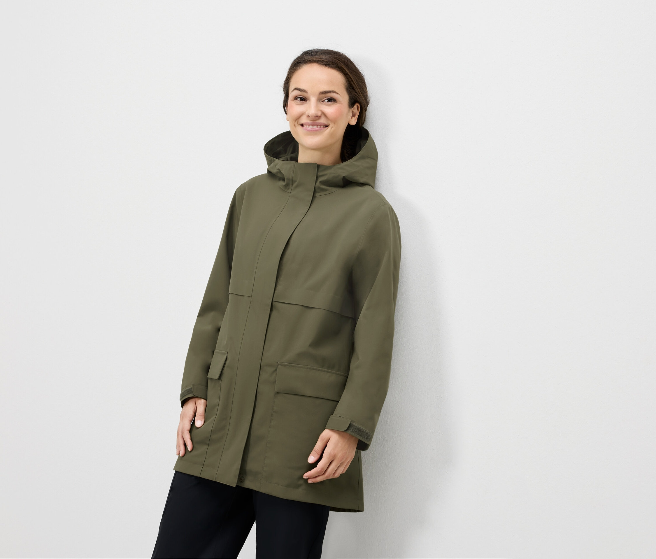 Frau posiert in olivgrüner Kapuzenjacke und schwarzer Hose.