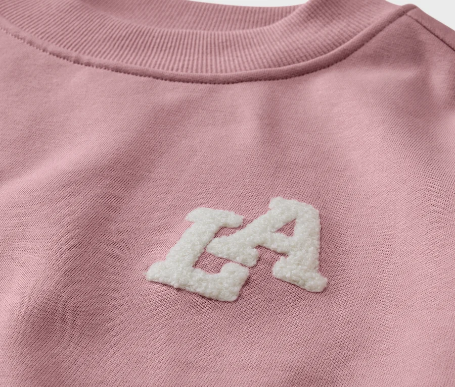 Detailansicht eines Kinder-Sweatshirts mit angerauter Innenseite in Rosa mit weißem "LA"-Schriftzug.