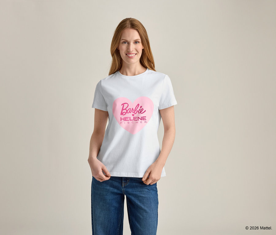 Frau mit blonden Haaren trägt ein weißes T-Shirt mit einem rosa Herzaufdruck und dem Schriftzug "Barbie HELENE FISCHER" darauf, dazu blaue Jeans.