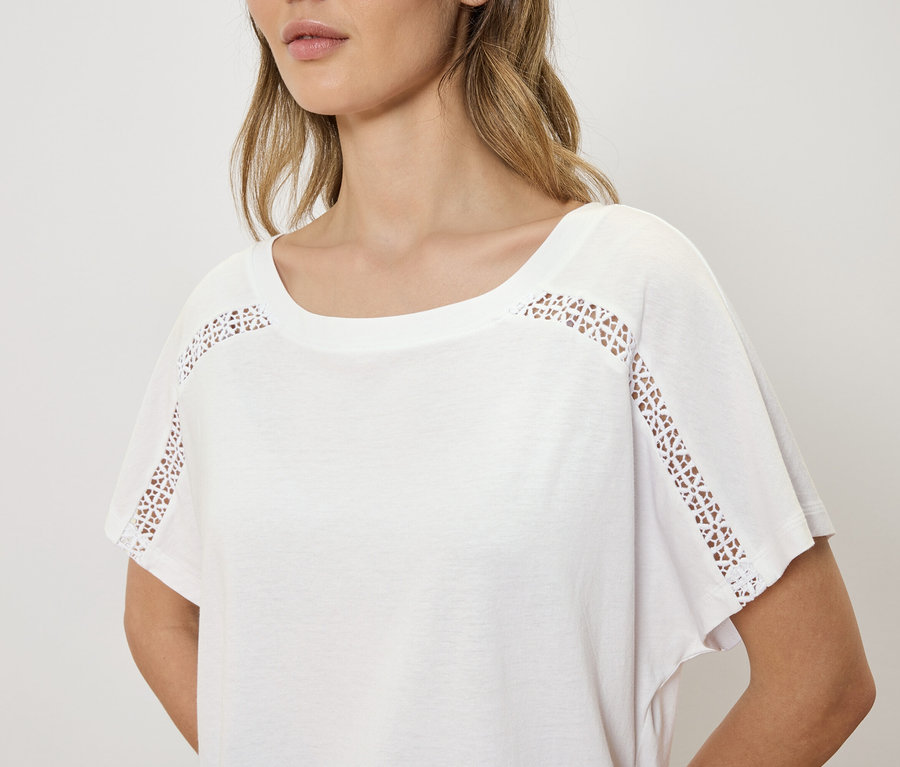 Frau trägt ein weißes T-Shirt mit Lochstickerei an den Schultern.