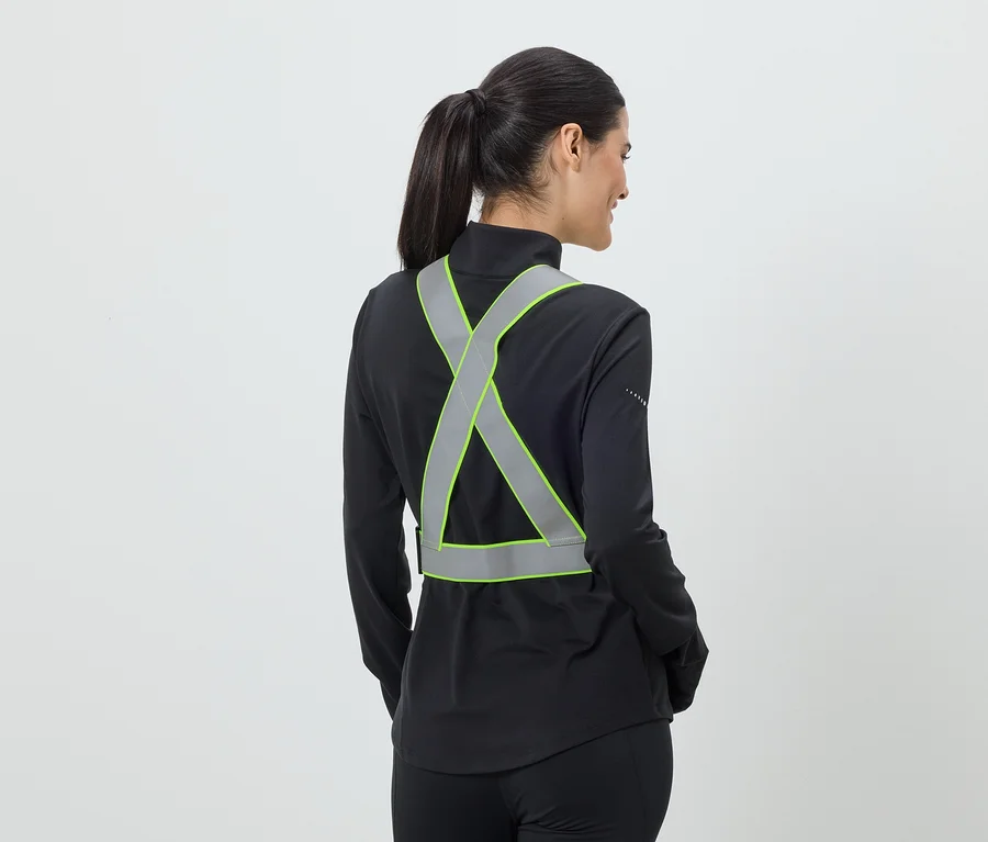 Frau mit Pferdeschwanz trägt eine reflektierende, neongrüne Sicherheitsweste über einer schwarzen Jacke.