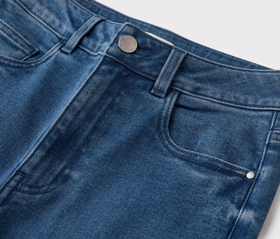 Nahaufnahme von blauen Jeans mit Knopf und Tasche vor einem weißen Hintergrund.