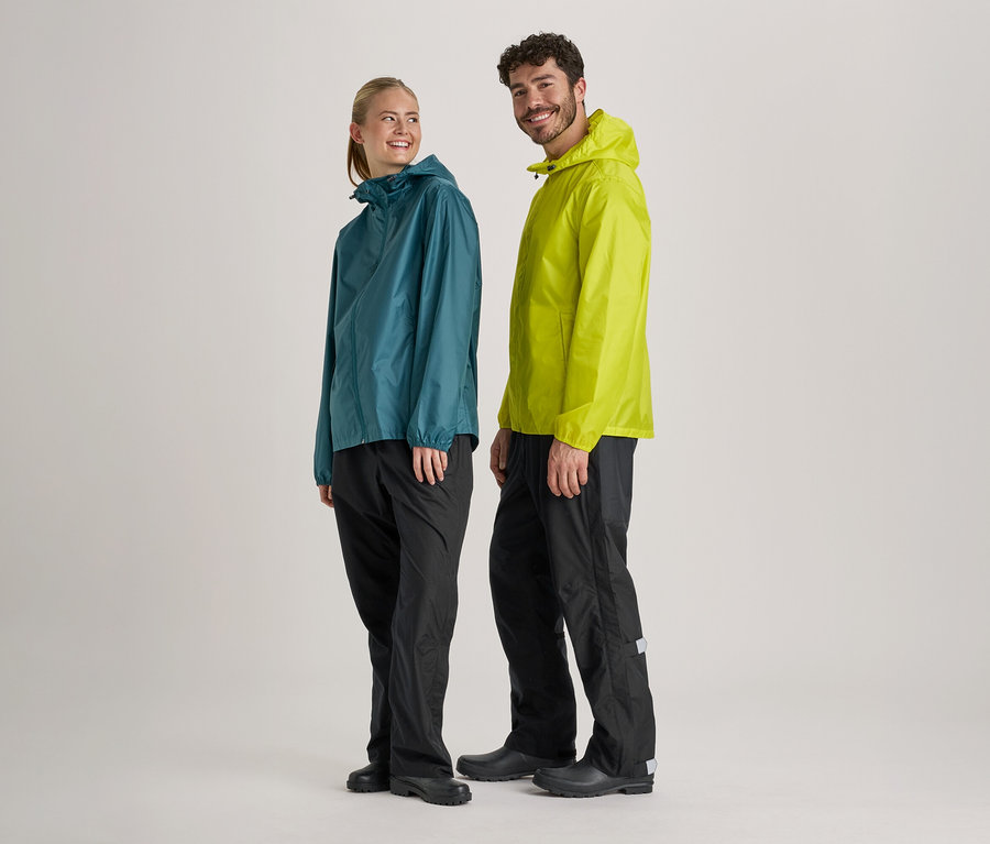Frau in blaugrüner und Mann in hellgrüner Regenjacke und schwarzer Regenhose stehen nebeneinander vor hellem Hintergrund.
