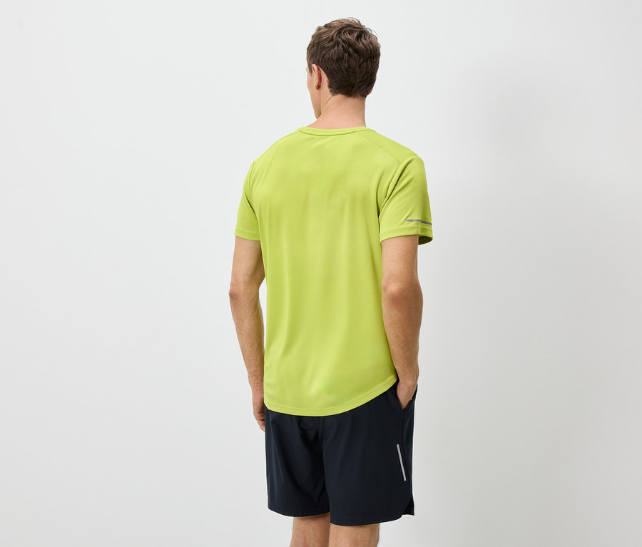 Rückansicht eines Mannes in einem hellgrünen T-Shirt und schwarzen Shorts vor einem weißen Hintergrund.