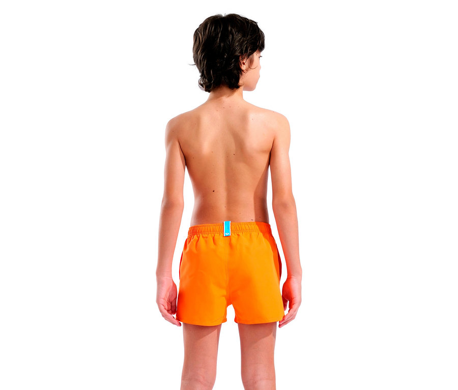 Rückansicht eines jungen Mannes mit dunklen Haaren, der orangefarbene Badeshorts vor einem weißen Hintergrund trägt.