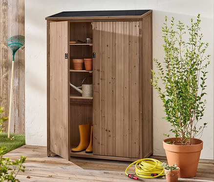 Ein offener Holzschrank steht draußen mit Gartengeräten, Töpfen, Gummistiefeln und einer Gießkanne im Inneren.