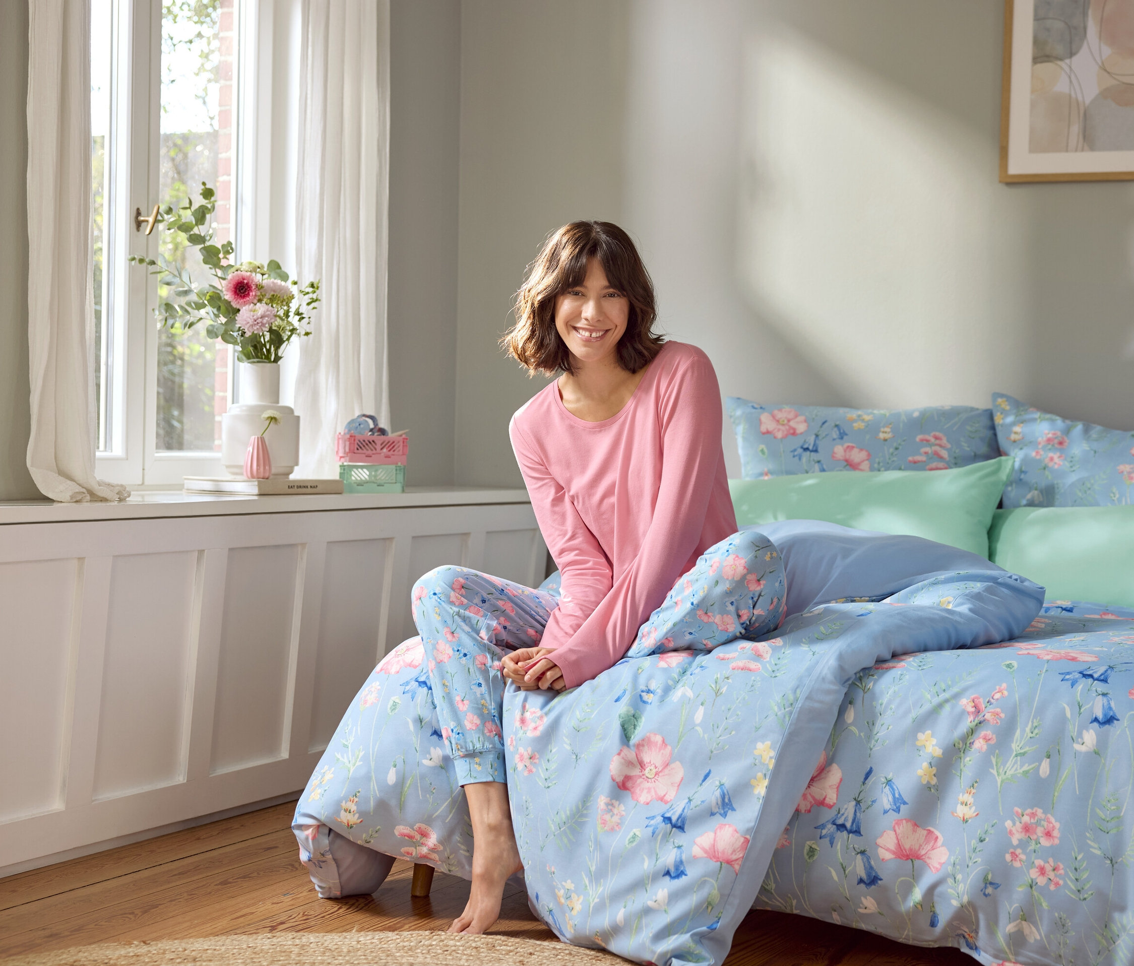 Frau sitzt auf einem Bett mit hellblauer Bettwäsche mit Blumenmuster.