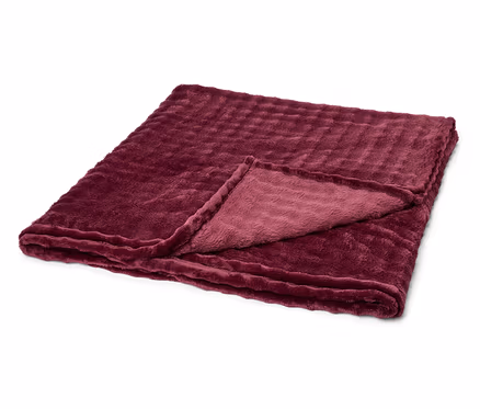 Eine gefaltete, weinrote Kuscheldecke mit gerippter Textur liegt auf einem weißen Hintergrund. Eine Ecke ist umgeschlagen.