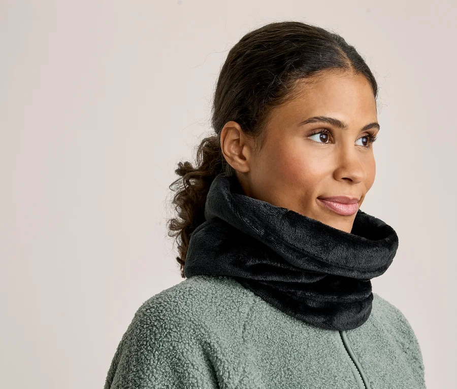 Eine Frau mit zurückgebundenem dunklem Haar trägt einen schwarzen flauschigen Halswärmer und eine hellgrüne Fleecejacke, während sie nach rechts blickt.