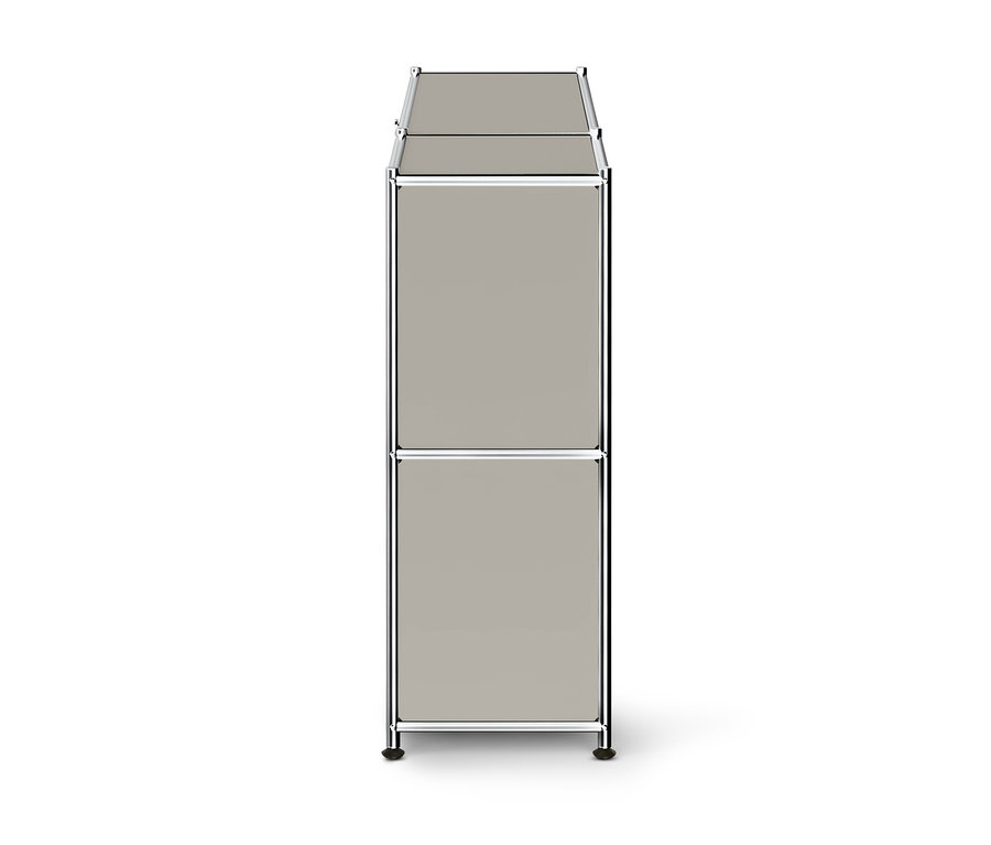 Ein hoher, schmaler, modularer Schrank mit zwei hellgrauen Fächern und einem Chromrahmen, der auf dunklen Füßen steht.