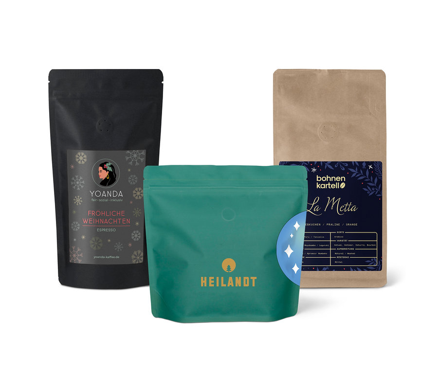 Drei Kaffeepackungen unterschiedlicher Marken stehen nebeneinander. Eine Packung ist schwarz mit Schneeflocken, eine ist grün und eine ist beige.