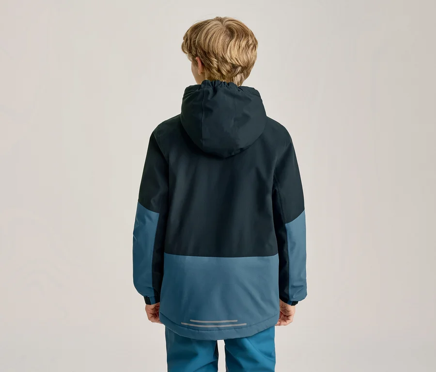 Kind von hinten gesehen, trägt eine zweifarbige Kapuzenjacke und passende Hose. Die Jacke ist oben dunkelblau, unten und an den Ärmeln hellblau, mit einem reflektierenden Streifen am Rücken.