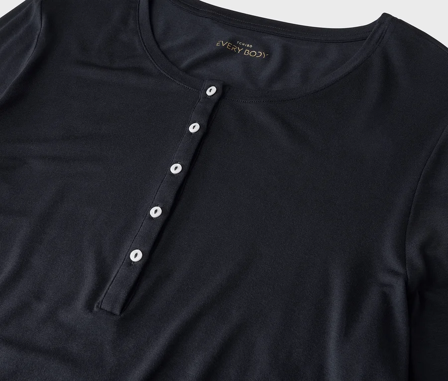 Dunkelblaues Langarmshirt mit Rundhalsausschnitt und Knopfleiste mit fünf weißen Knöpfen. Im Nacken ist das Label "TCHIBO EVERY BODY" sichtbar.