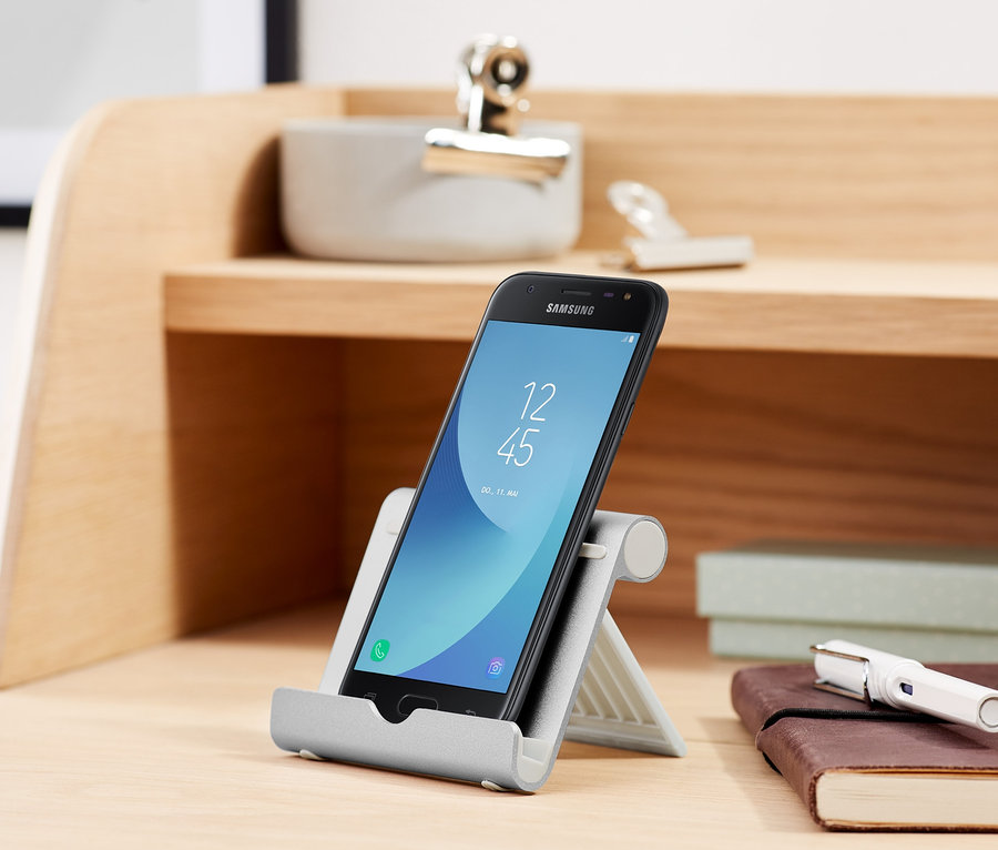 Schwarzes Smartphone steht in einer Smartphone- und Tablet-Halterung auf einem Schreibtisch.
