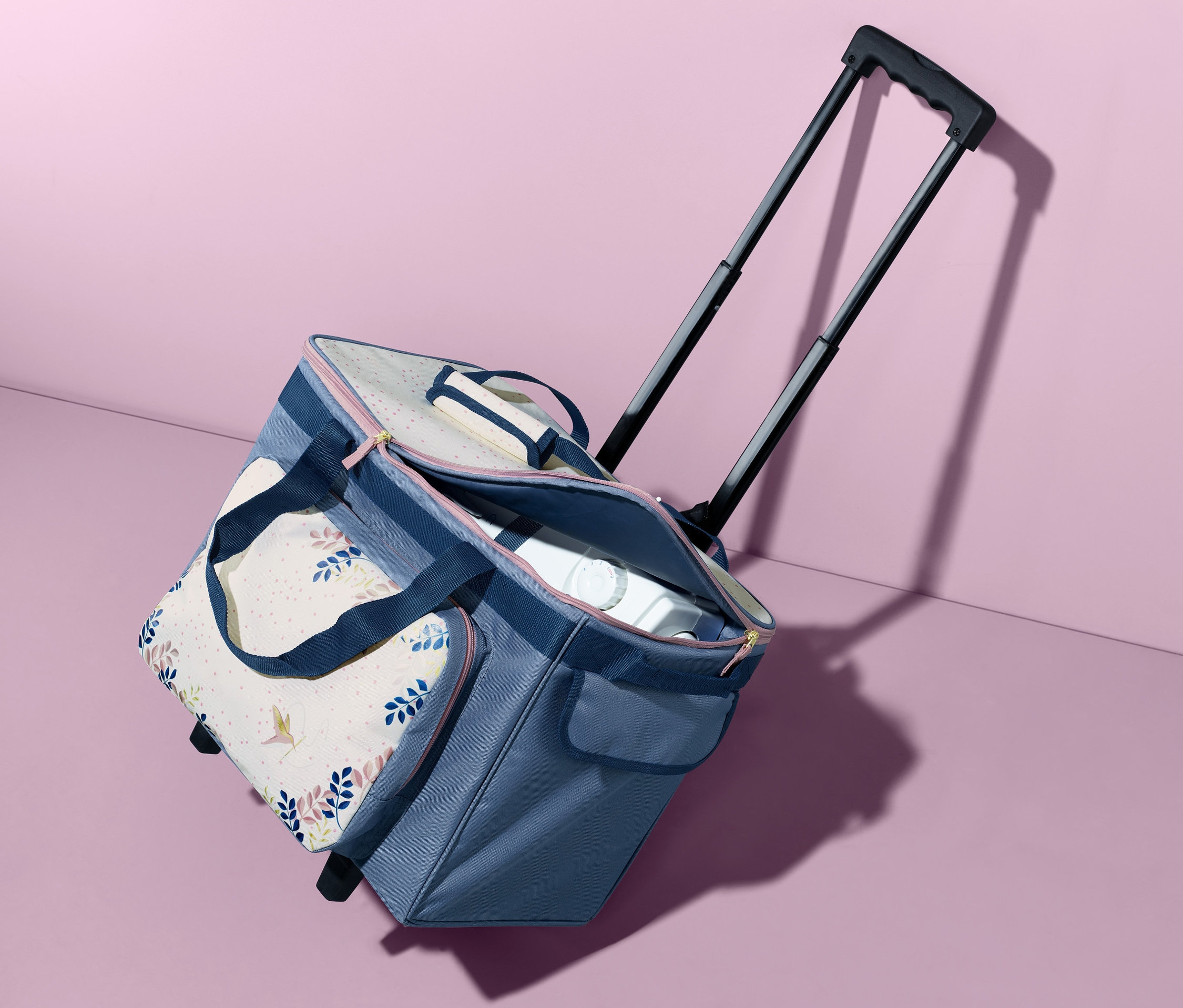 Ein blauer Nähmaschinen-Trolley steht vor einem rosa Hintergrund.