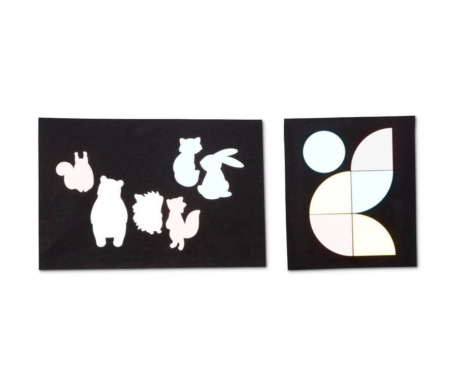 Zwei schwarze Blätter mit reflektierenden Aufklebern von Tieren und geometrischen Formen.