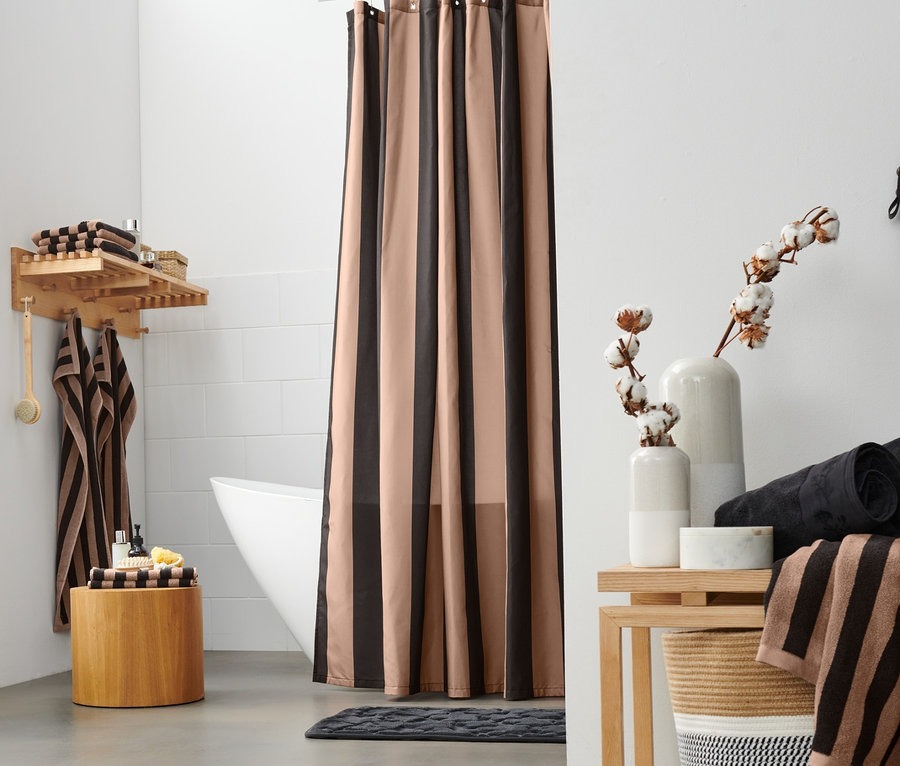Im Badezimmer befinden sich eine Leiter mit einem schwarz-braunen Handtuch mit Blumenmuster, ein Fenster, ein Korb, ein Textilvorhang, zwei schwarze Premium-Handtücher, ein schwarz-braun gestreiftes, hochwertiges Badetuch und beige Premium-Handtücher.