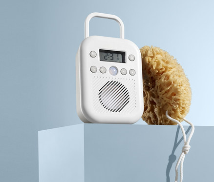 Auf einem blauen Sockel stehen ein weißes Badradio und ein Naturschwamm.
