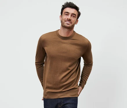Mann posiert vor weissem Hintergrund mit einem cognacfarbenen Merino-Pullover.