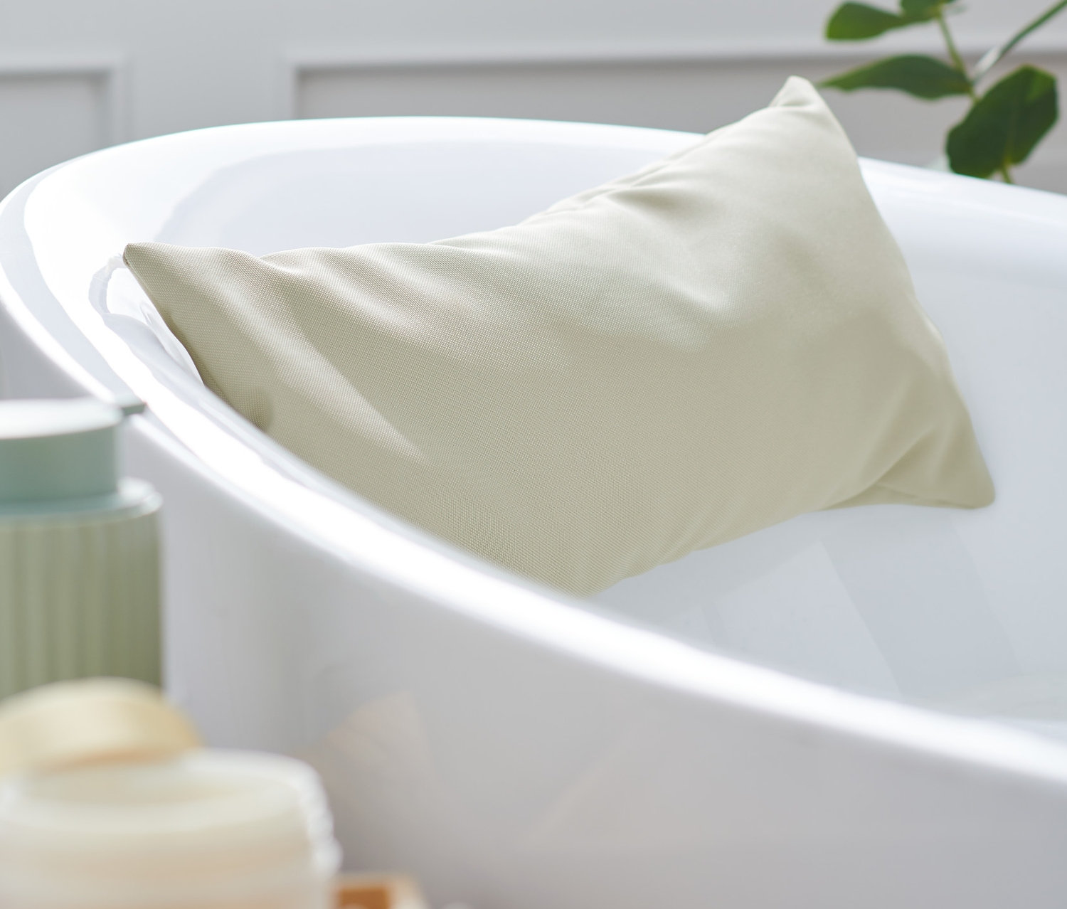 Ein beiges Badewannenkissen lehnt in einer weißen Badewanne.