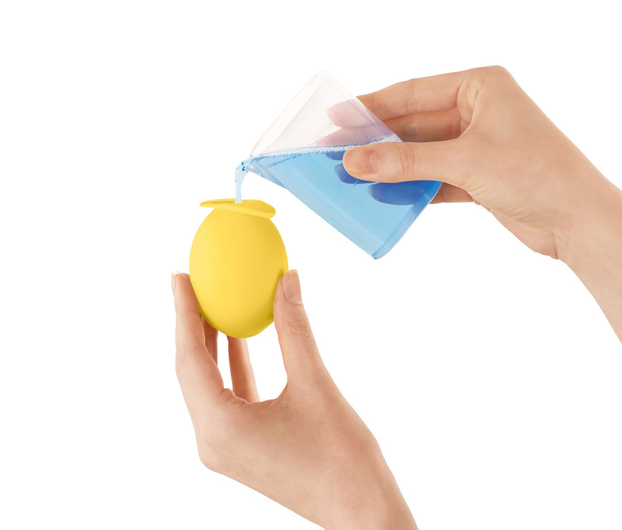 Frau gießt blaue Flüssigkeit aus einem Messbecher in einen gelben Wasserhahn Entkalker-Aufsatz.