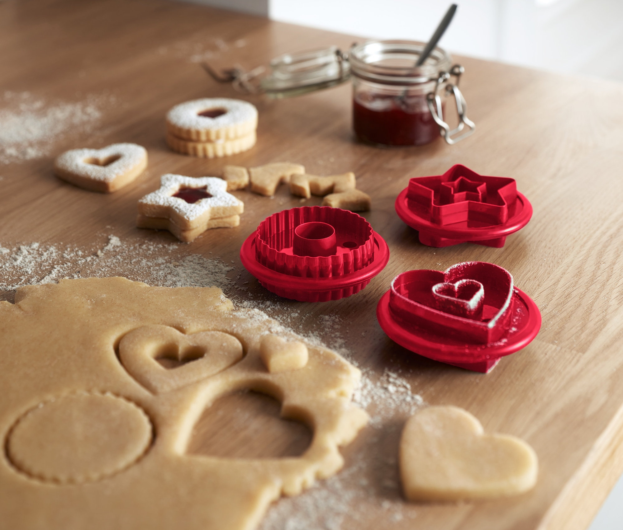 Auf einem Holztisch liegen Linzer Plätzchen und 3 Linzer-Plätzchen-Ausstecher.