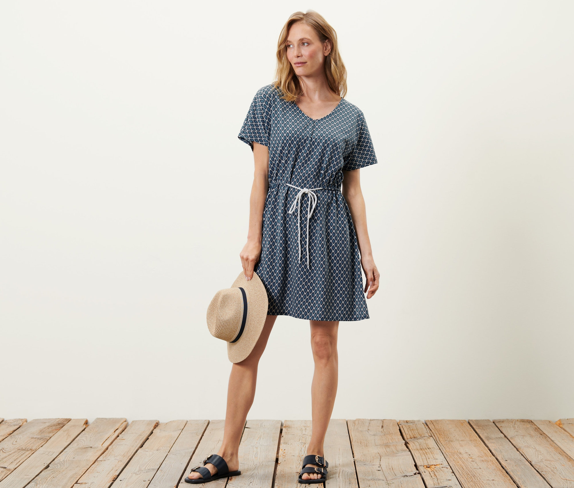 Frau posiert in Strandtunika und hält einen Hut.