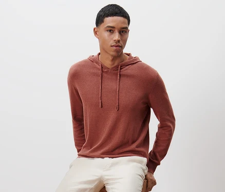 Mann sitzt auf einem Holzhocker und trägt einen Strick-Hoodie.