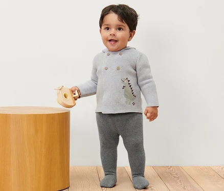 Ein Junge steht und hält ein Holzspielzeug, er trägt eine melierte Baby-Thermostrumpfhose.