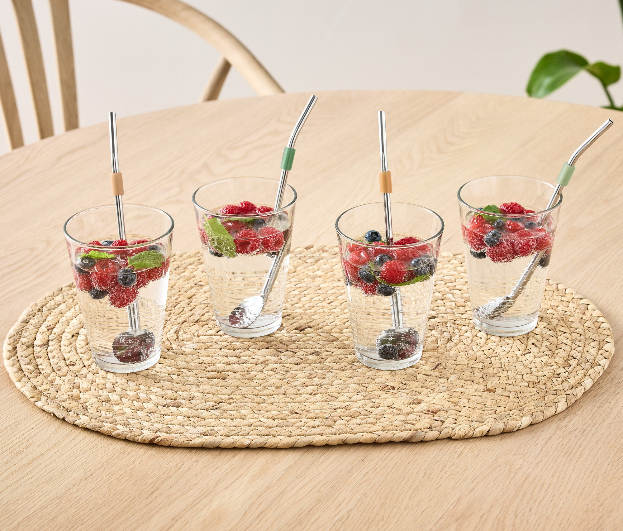 Vier Gläser mit Wasser, Früchten und 4 Löffel auf einem Tisch.