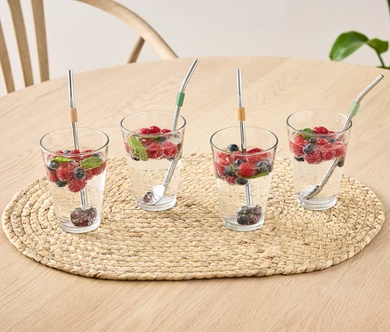 Vier Gläser mit Wasser, Früchten und 4 Löffel auf einem Tisch.