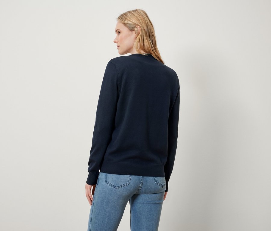 Blonde Frau mit dem Rücken zur Kamera trägt einen dunkelblauen Pullover und Jeans.