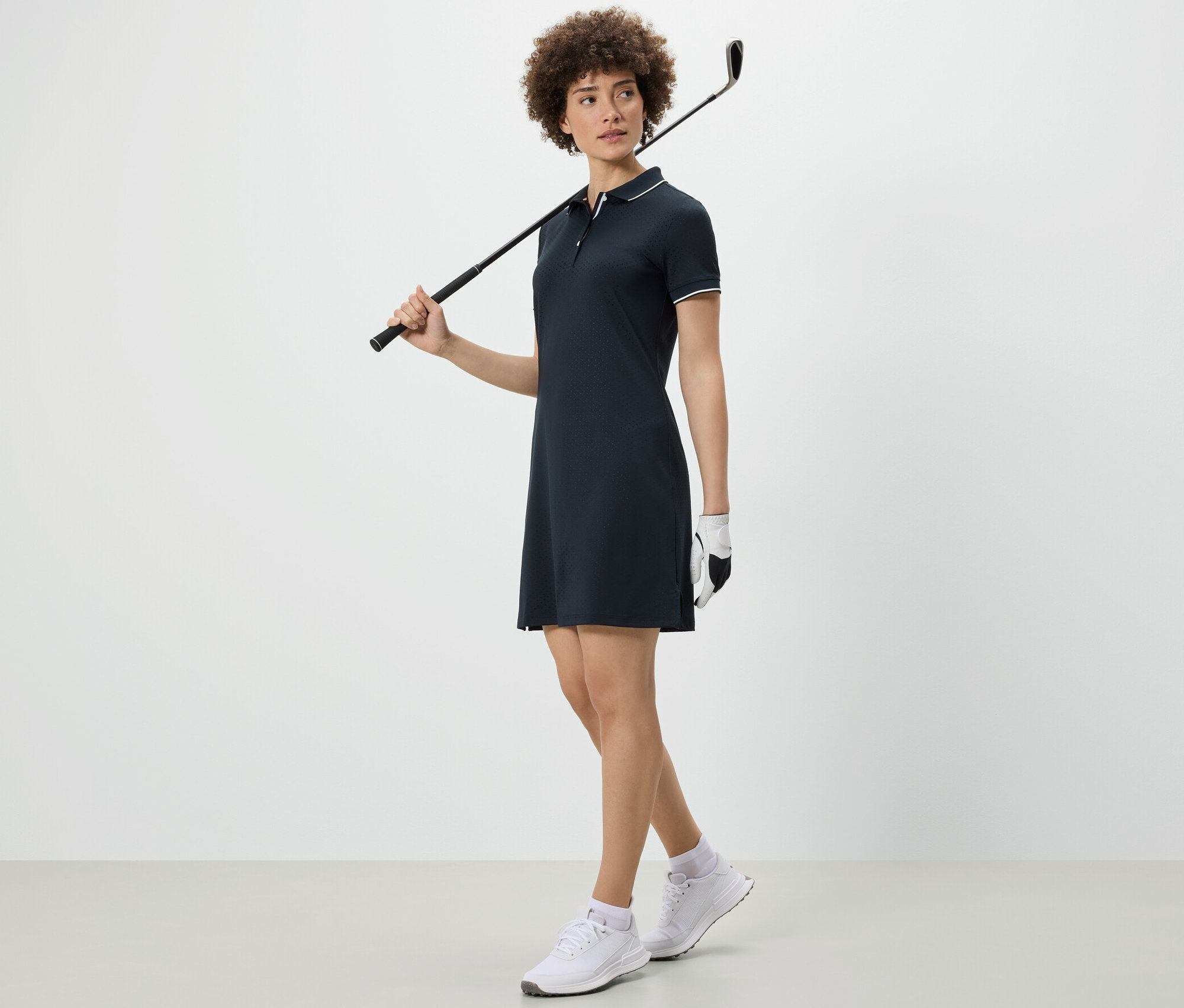 Frau hält Golfschläger über der Schulter und trägt ein Sportkleid.