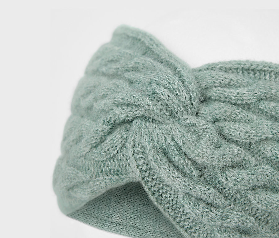 Nahaufnahme eines hellblauen, gestrickten Stirnbands mit Zopfmuster.