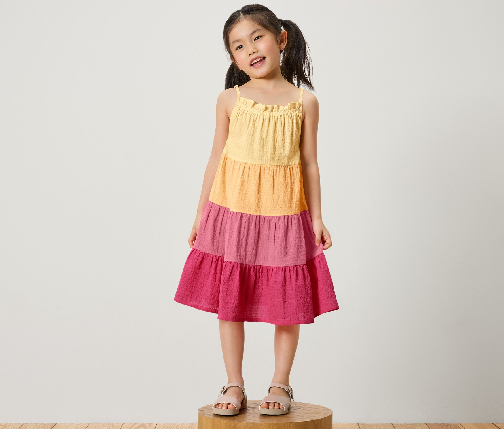 Mädchen steht auf einem Holzsockel und trägt ein Kinder-Webkleid.