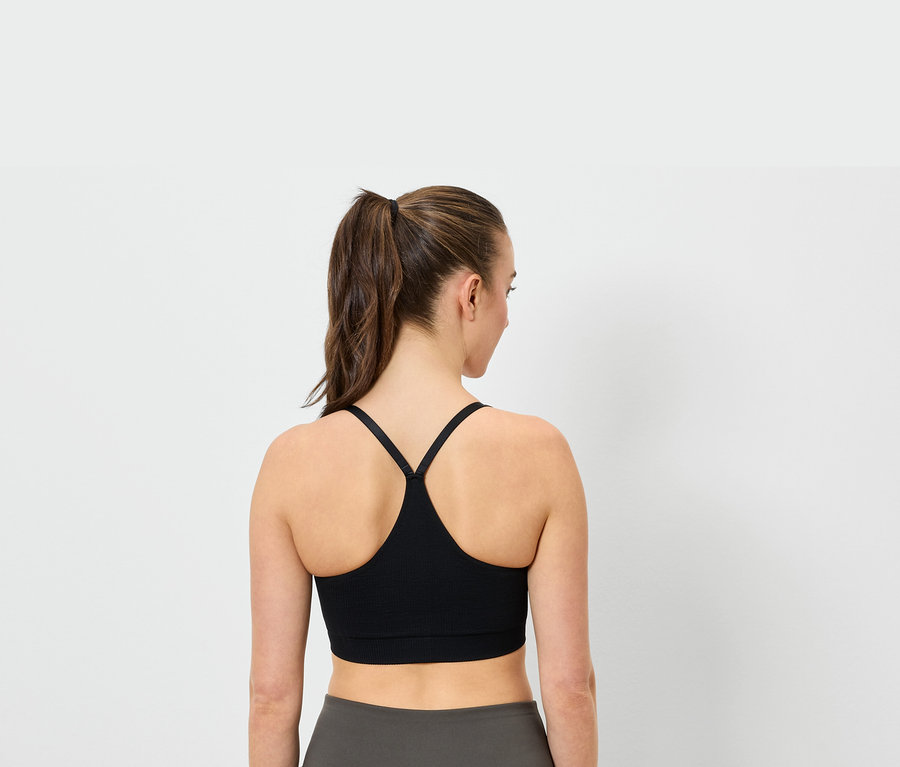 Rückansicht einer Frau mit Pferdeschwanz, die einen schwarzen Sport-BH und graue Leggings trägt.