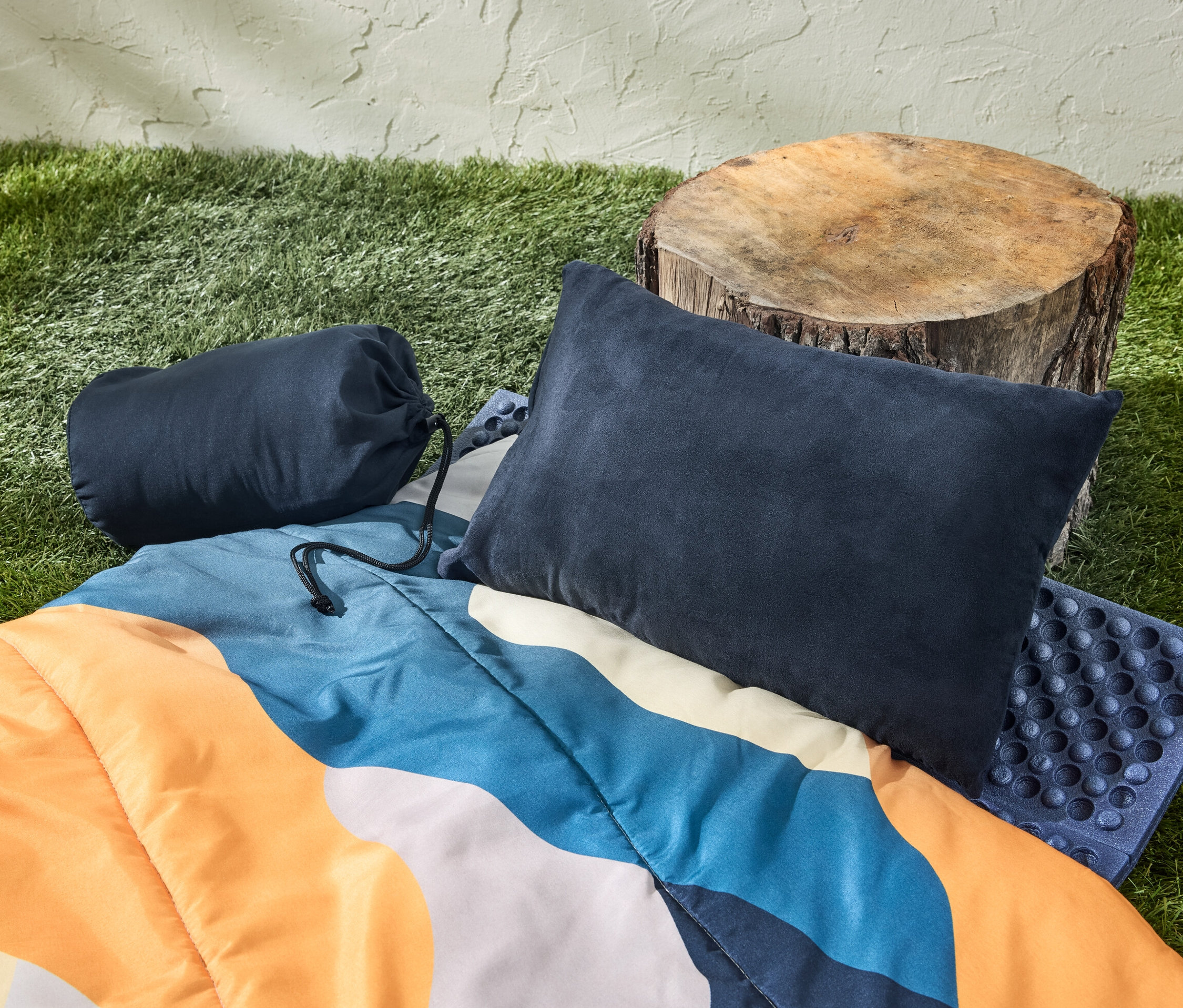 Camping-Kissen, Schlafsack und Baumstumpf auf Gras.