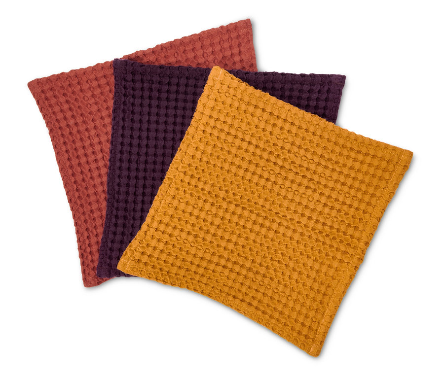Drei farbige Stoffservietten mit Textur in den Farben Orange, Lila und Braunrot liegen auf einem weißen Hintergrund.