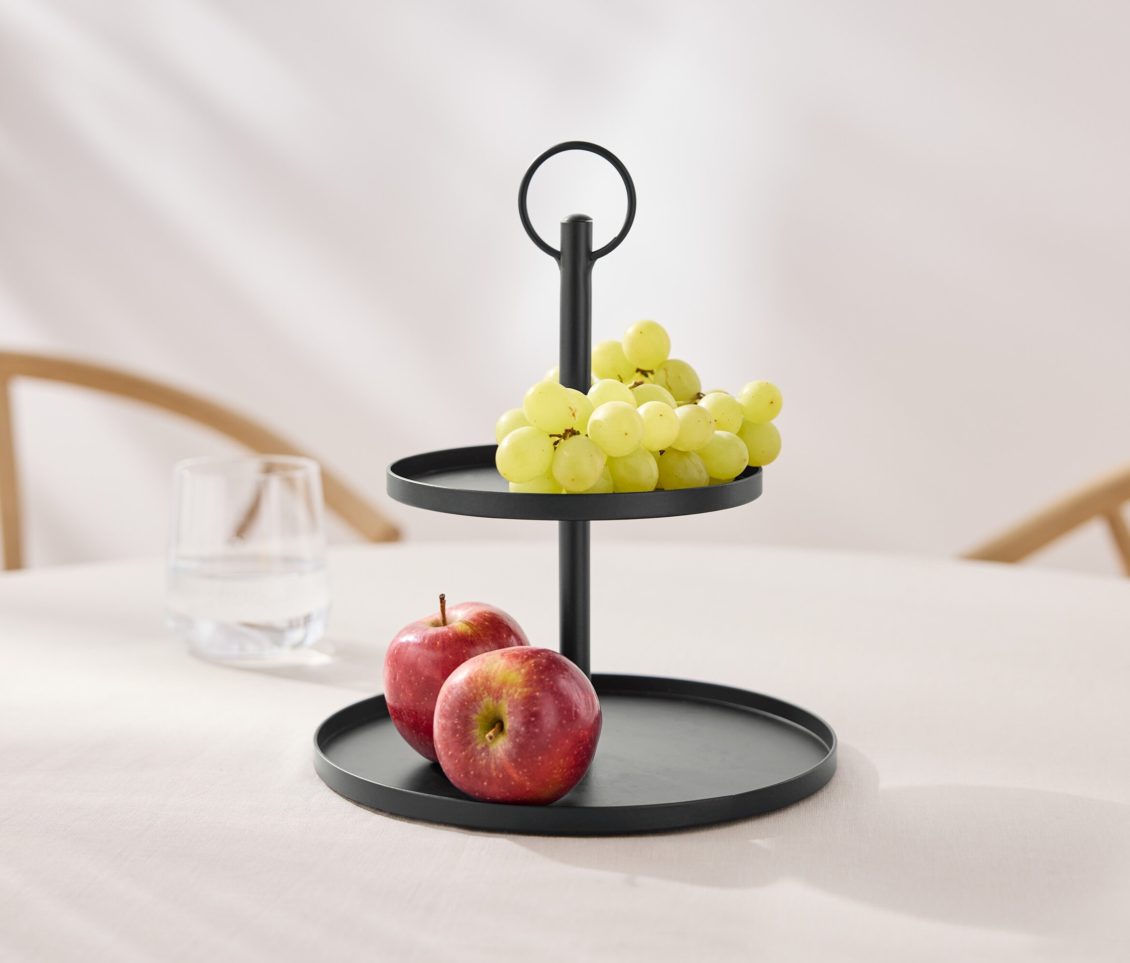 Ein zweistöckiger, schwarzer Etagere mit Trauben und Äpfeln auf einem Tisch.