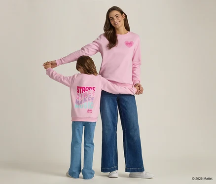 Eine Frau und ein Kind halten Händchen, beide tragen passende rosa Sweatshirts und Jeans.