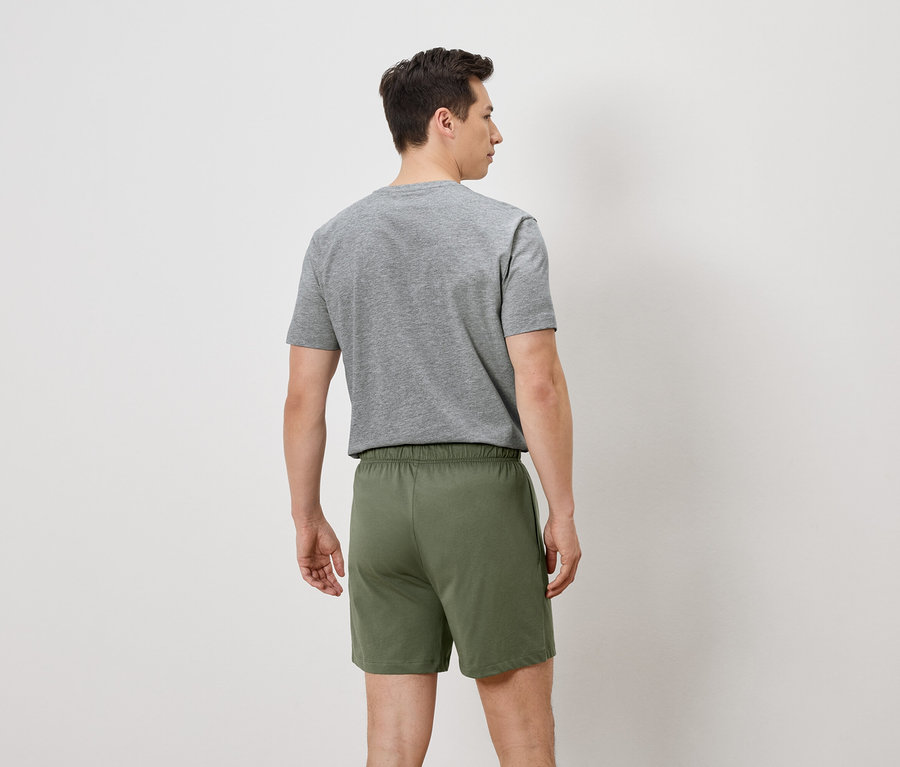Rückansicht eines Mannes mit grauem T-Shirt und grünen Shorts vor einem weißen Hintergrund.