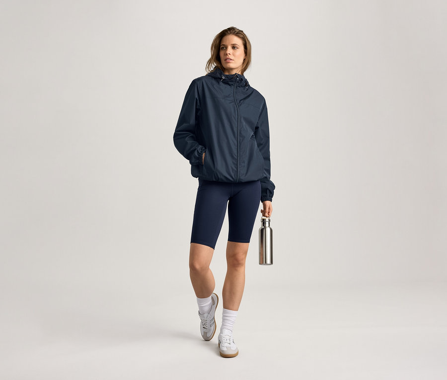 Frau mit Regenjacke, Radlerhose und Trinkflasche. Sie trägt Socken und Turnschuhe.