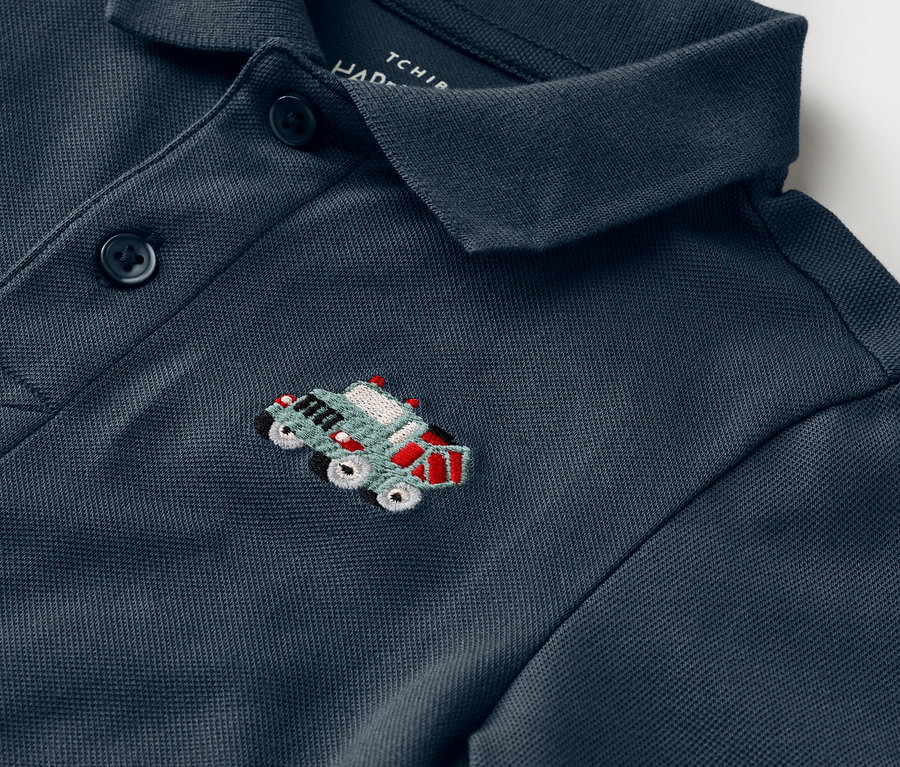 Nahaufnahme eines marineblauen Poloshirts mit einer kleinen, gestickten Abbildung eines grünen Jeeps mit roten Akzenten.