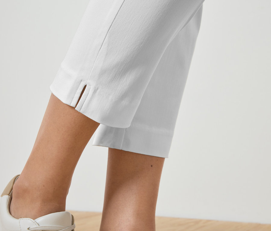 Nahaufnahme der Beine einer Person, die weiße Hosen und dazu passende Turnschuhe trägt.