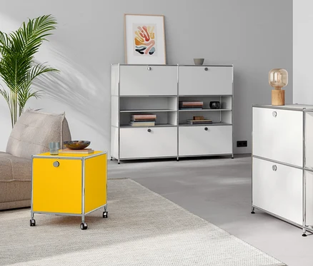 Wohnzimmer mit Tischleuchte aus Holz auf einer Kommode Metall »CN3« mit 4 Klappenfächern, weiß. Gelber Beistelltisch Metall »CN3« mit Klappfach.