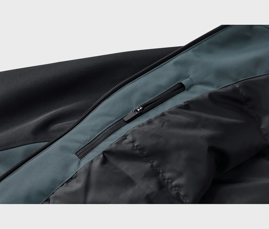 Nahaufnahme einer schwarz-dunkeltürkisen Jacke, die einen schwarzen Reißverschluss mit Zipper und eine kleinere, versteckte Reißverschlusstasche auf dem dunkeltürkisen Einsatz neben einem gesteppten schwarzen Futter zeigt.