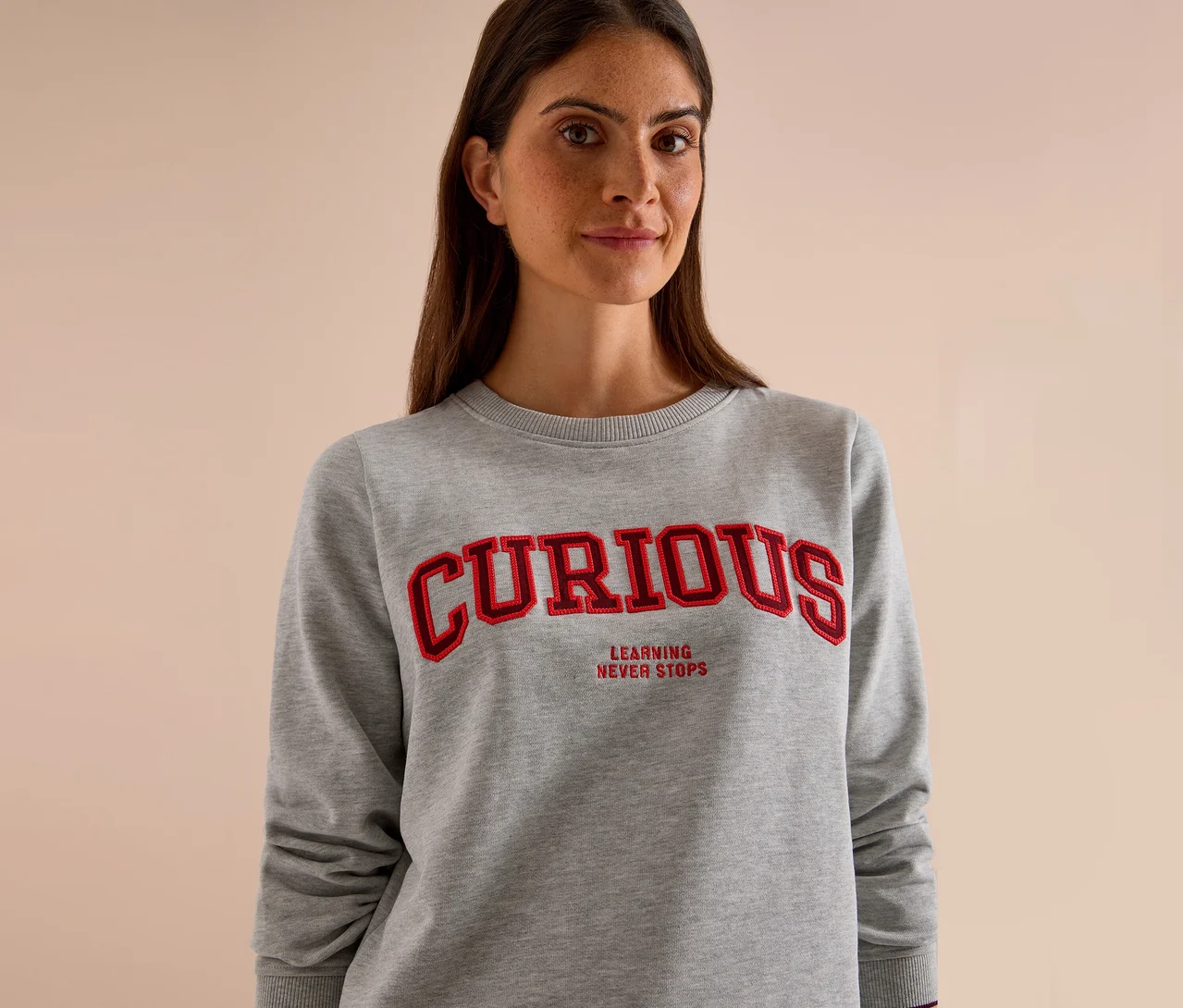 Frau trägt ein graues CECIL Sweatshirt mit rotem "CURIOUS" Schriftzug und "LEARNING NEVER STOPS".